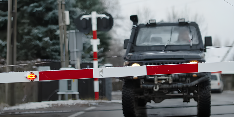 Widok na samochód na przejeździe, przed nim opuszczona rogatka