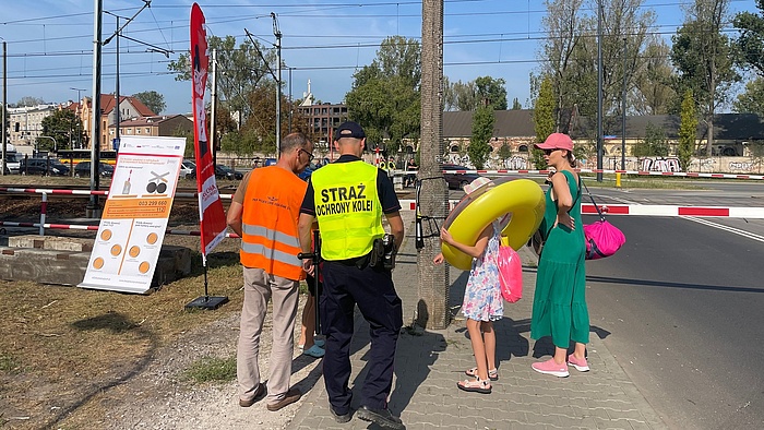 Przedstawiciel PLK SA i Straży Ochrony Kolei przekazują materiały edukacyjne matce z dziećmi na przejeżdzie kolejowo-drogowym, fot. Anna Znajewska-Pawluk