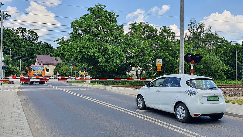 Przejazd kolejowo-drogowy zamkniętymi rogatkami. Samochody przed szlabanem.