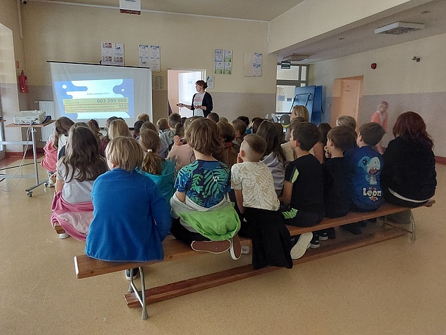 Prelekcja w szkole podstawowej - prowadząca przy ekranie i grupa dzieci.