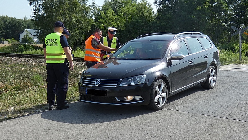 Policjant, funkcjonariusz SOK i przedstawiciel kampanii  wręczają ulotkę kierowcy w samochodzie.