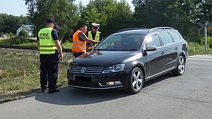 Policjant, funkcjonariusz SOK i przedstawiciel kampanii  wręczają ulotkę kierowcy w samochodzie.
