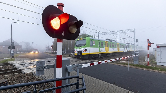 Przejazd z opuszczonymi szlabanami i sygnalizatorem, przejeżdżający pociąg.