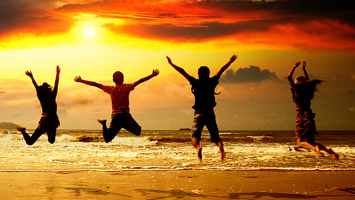 4 osoby skaczą na tle morza i zachodzącego słońca.