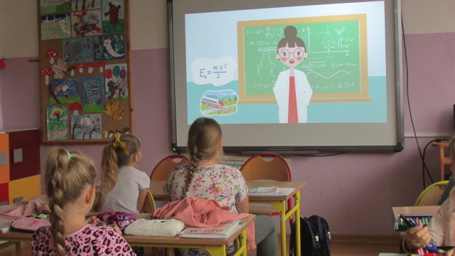 Dzieci w ławkach szkolnych oglądające filmik edukacyjny na ekranie