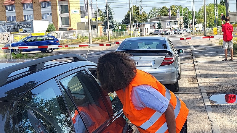 Koordynator wręcza ulotki kierowcy przed zamkniętym przejzadem.