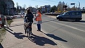 Pracownicy PLK oraz funkcjonariusze Straży Ochrony Kolei rozmawiają z kierowcami i rowerzystami na przejeździe kolejowo-drogowym w ramach akcji edukacyjnej kampanii „Bezpieczny przejazd”. Widoczne auta, pociąg i rozmówcy.