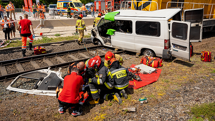 Strażacy i ratownicy opatrują rannego z wraku pojazdu, który zderzył się z lokomotywą na przejeździe - zdjęcie z symulacji.