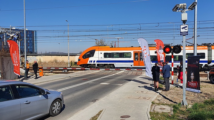 Akcja ulotkowa na przejeździe kolejowym w Krakowie, zamknięty szlaban i przejeżdżający pociąg