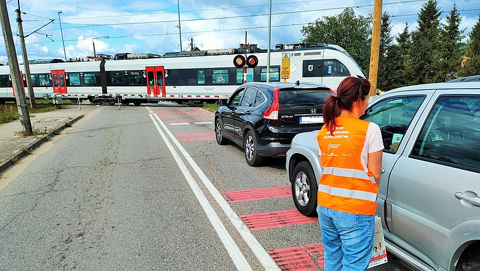 Koordynator kampanii podczas akcji ulotkowej, przejazd kolejowy, pociąg na torach