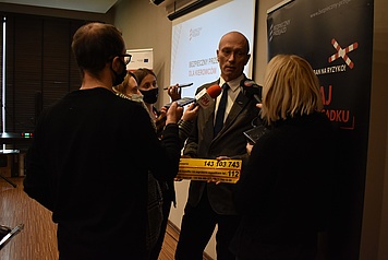 M. Kruszyński trzymający żółtą naklejkę PLK udzielający wywiadu mediom. 