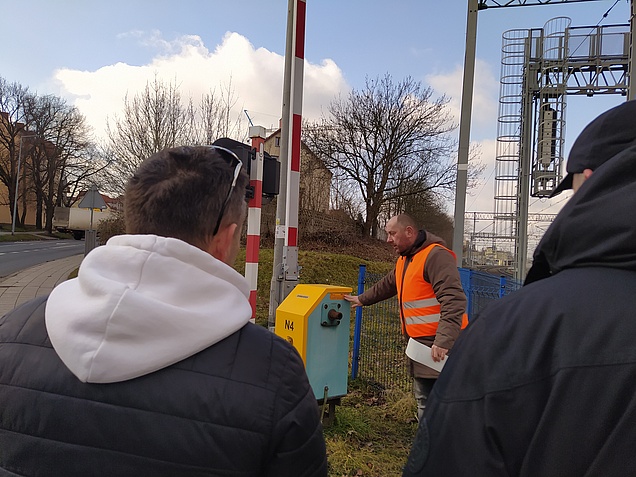 Instruktor pokazuje zasadę działania żółtej naklejki, na pierwszym planie 2 uczestników stojących tyłem.