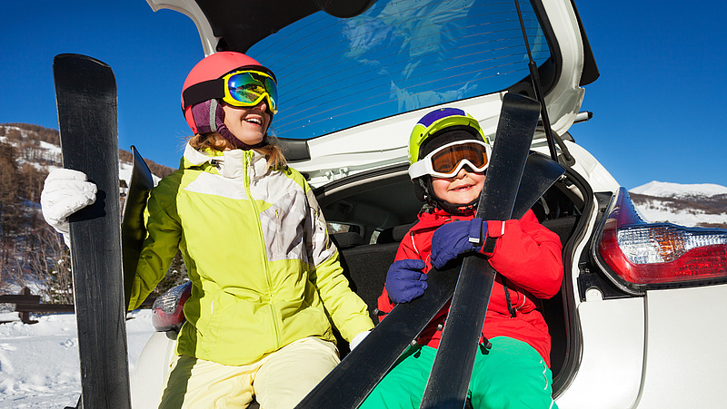 Dwoje dzieci z nartami opartych o bagażnik samochodu