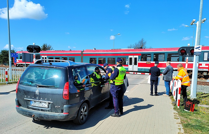 Samochód przed przejazdem, funkcjonariusze SOK rozdają ulotki, w tle pociąg. fot. Przemysław Zieliński PKP PLK