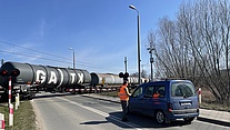 Pracownicy PLK oraz funkcjonariusze Straży Ochrony Kolei rozmawiają z kierowcami i rowerzystami na przejeździe kolejowo-drogowym w ramach akcji edukacyjnej kampanii „Bezpieczny przejazd”. Widoczne auta, pociąg i rozmówcy.