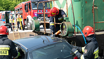Trzech strażaków pracuje przy warku samochodu podczas symulacji wypadku.