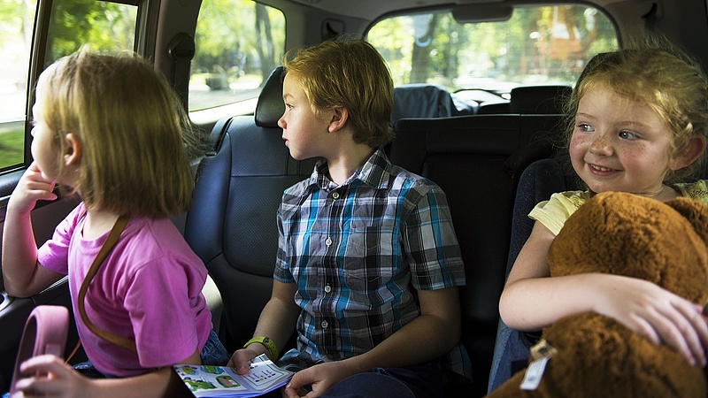 Trójka dzieci siedząca na tylnych siedzeniach w samochodzie.
