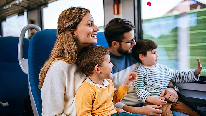 Rodzina z dwójką dzieci na kolanach podróżują pociągiem