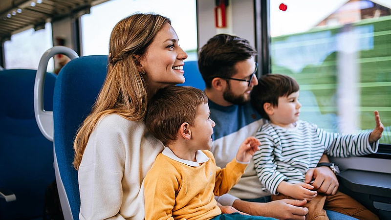 Rodzina z dwójką dzieci na kolanach podróżują pociągiem