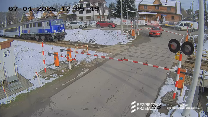 Samochód na który opadły rogatki, pociąg tuż przed przejazdem.