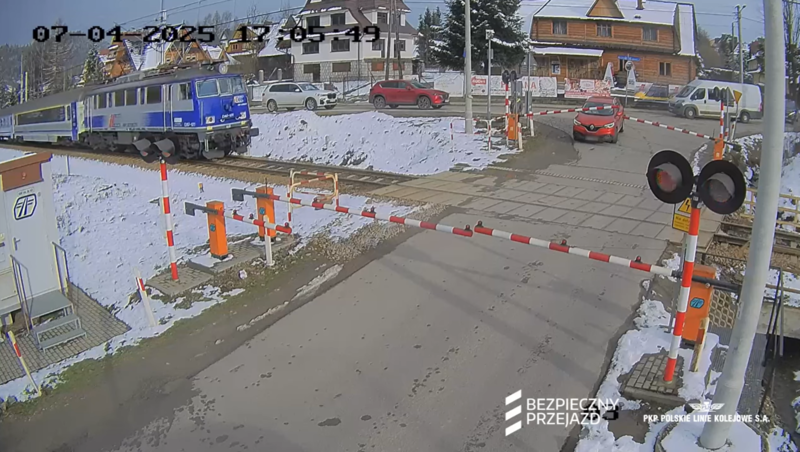 Samochód na który opadły rogatki, pociąg tuż przed przejazdem.