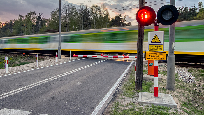 Przejazd kolejowy. Migająca sygnalizacja, zamknięte rogatki - pociąg pędzący przez przejazd.