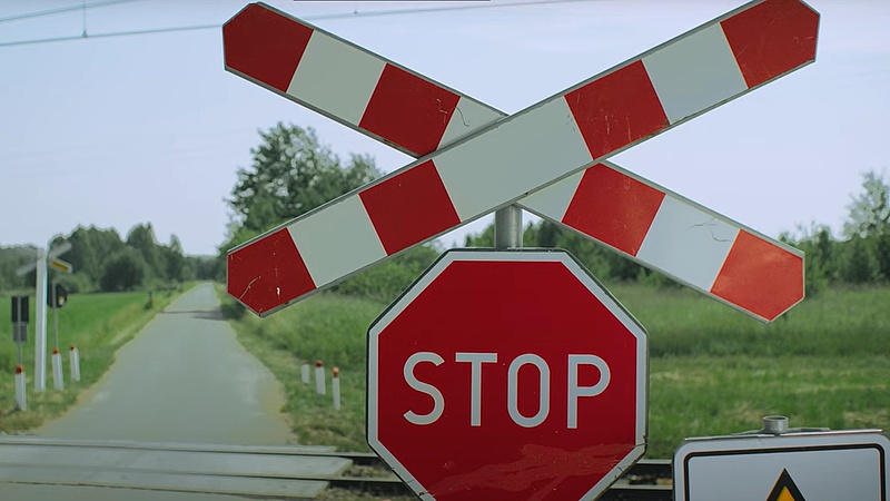 Krzyż św. Andrzeja, znak STOP, w tle przejazd i droga