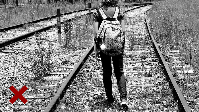 Dziewczynka z plecakiem idzie po torach kolejowych.
