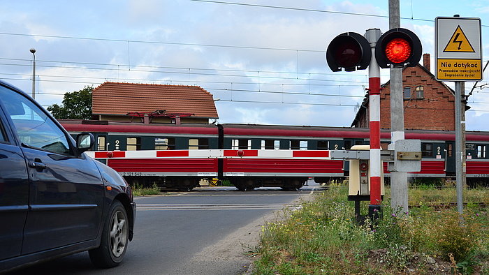 Samochód przed przejazdem, rogatki zamknięte, pociąg na torach.