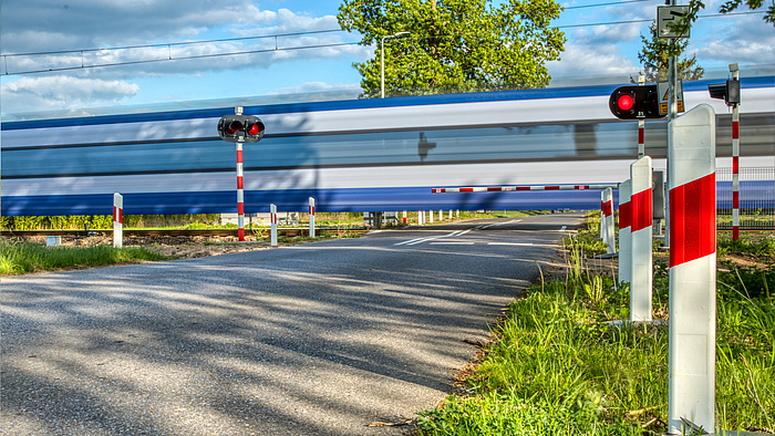 przejazd kolejowo-drogowy, zamknięta rogatka, w tle przejeżdżający pociąg