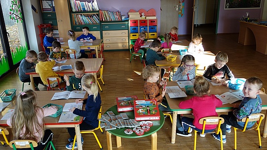 Przedszkolaki siedzące przy stolikach podczas korzystania z materiałów edukacyjnych kampanii.
