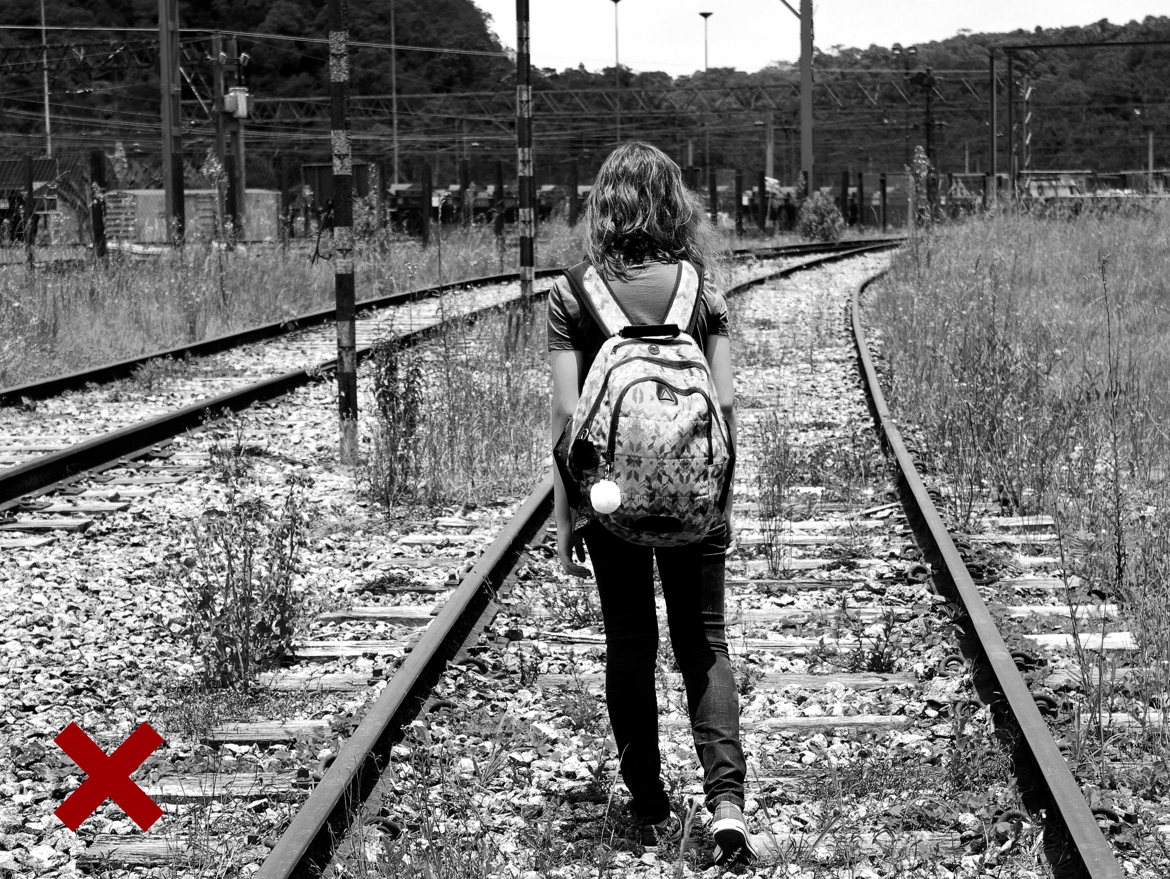 Dziewczynka z plecakiem idzie po torach kolejowych.